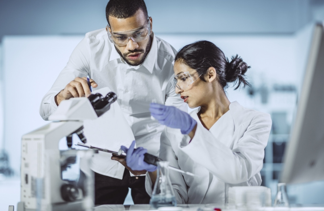 Two scientists examining and taking notes on samples being analyzed under a microscope