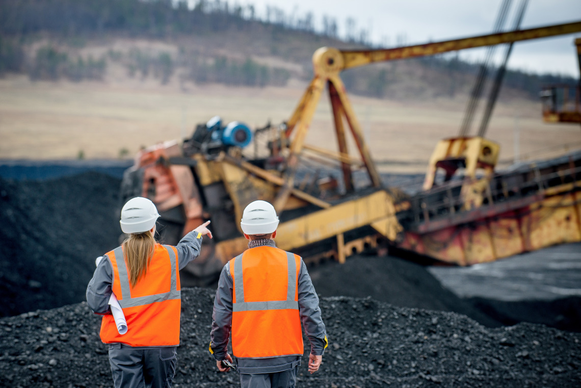 Two mining workers looking at large mining equipment in use