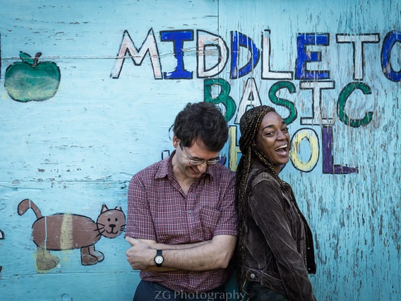 Man and woman stand laughing in front of blue school building