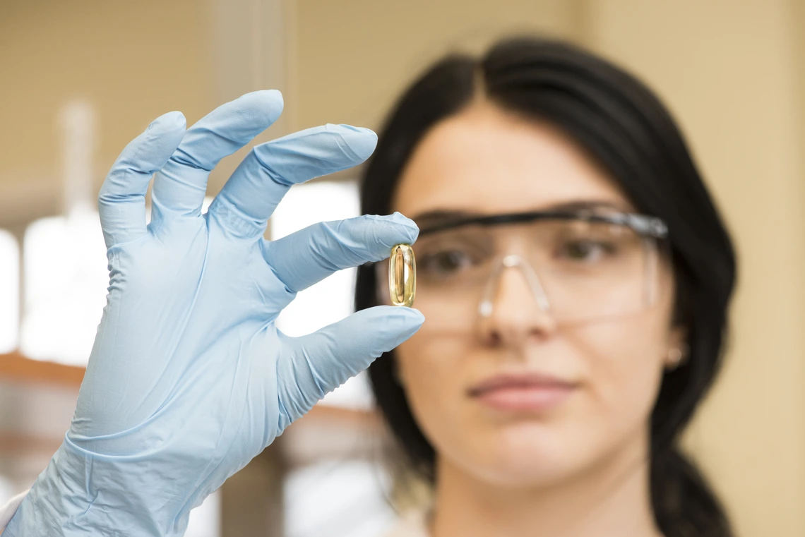 A scientist closely inspecting a pill with gloves and safety goggles on