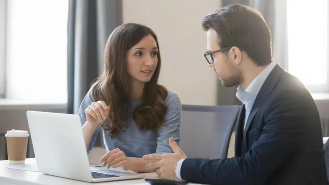 Two economics professionals discussing work next to a laptop
