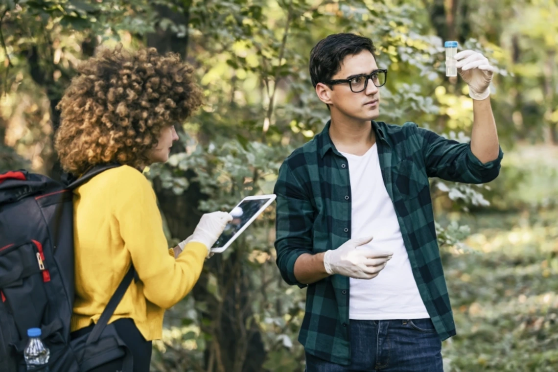 Two students in a forest examining a sample