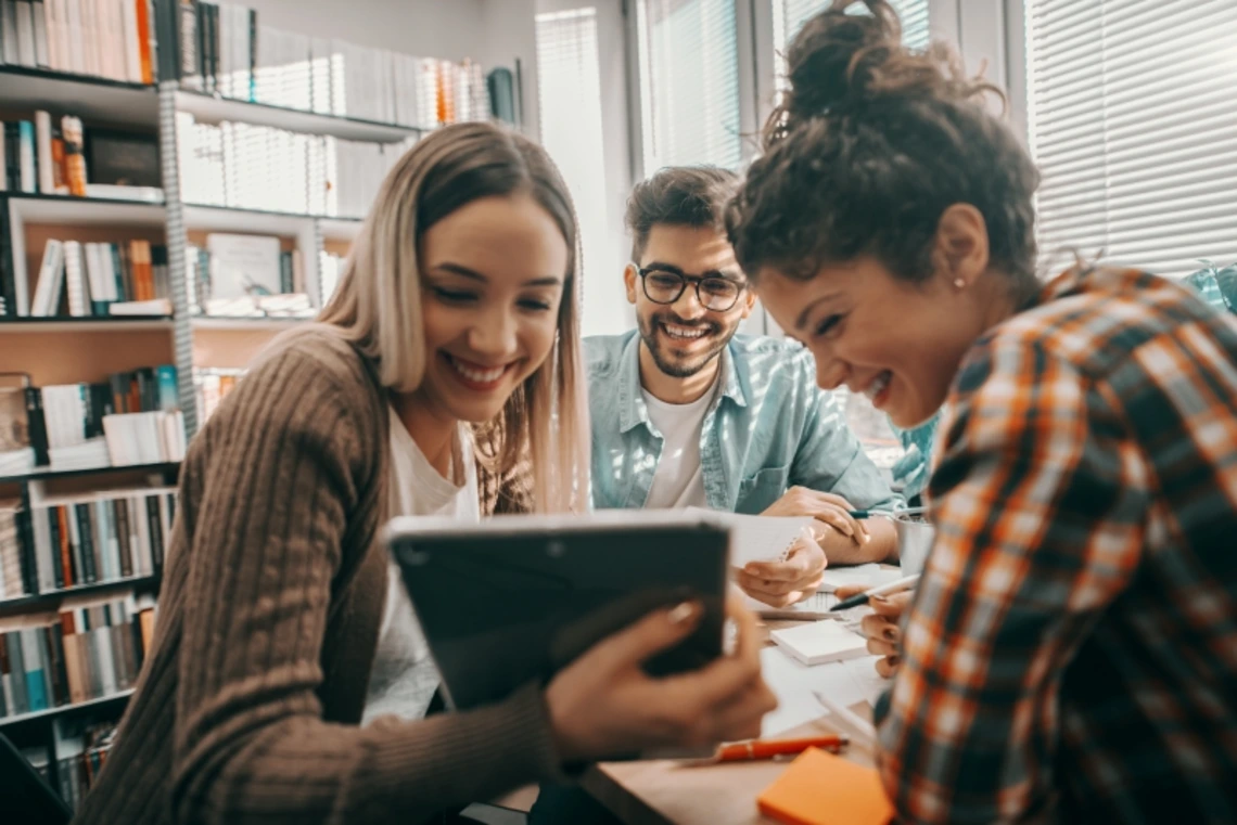 Three students looking happily at data on a tablet