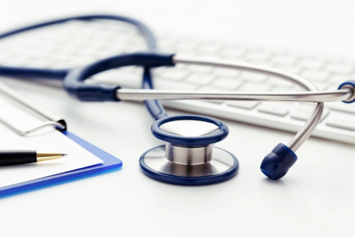 A stethoscope, keyboard, and a clipboard with a pen resting on top