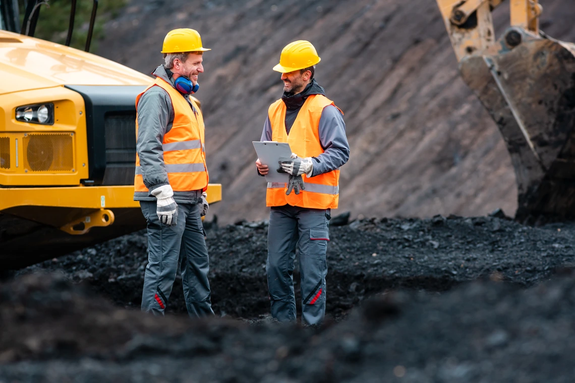 Worker with a clipboard discussing things with another worker in quarry