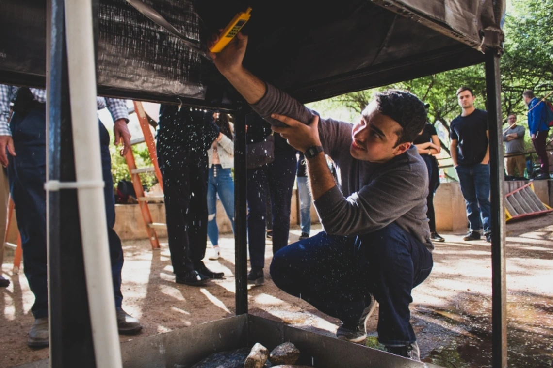 A man using a tool to inspect a structure he's kneeling under