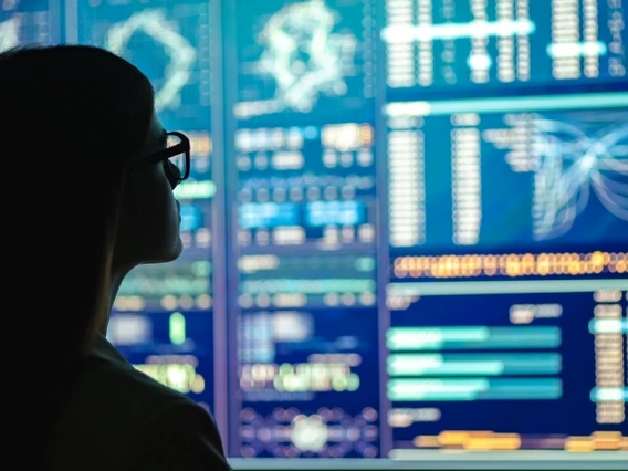 A silhouetted woman with glasses looking at a large computer screen with data visualization analytics displayed