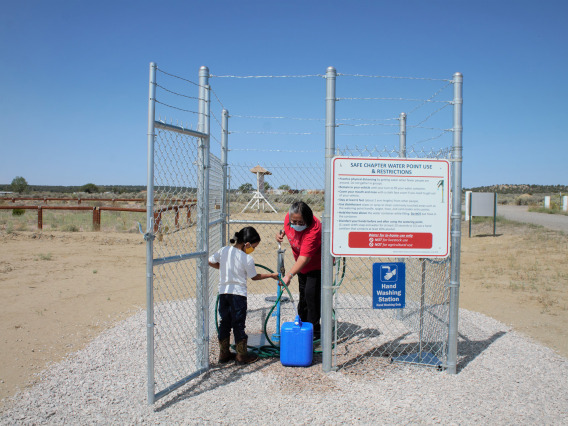 An image of a mother and daughter filling a container with water from a safe water point in the Navajo Nation