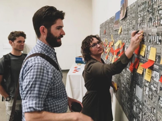 Three people looking at a wall-mounted map and writing notes