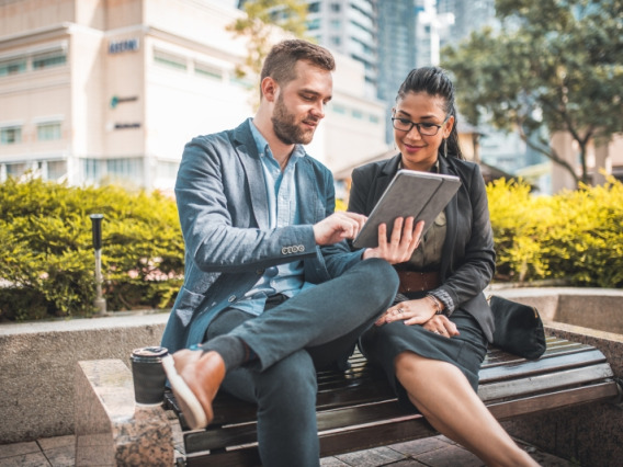 A man and woman looking at a tablet together on a park bench