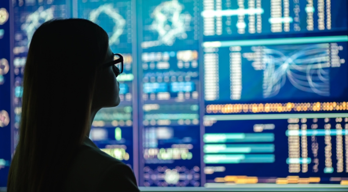 A silhouetted woman with glasses looking at a large computer screen with data visualization analytics displayed