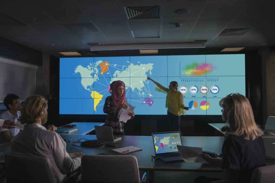 People in a conference room listening to a presentation with geographical data projected on a screen.