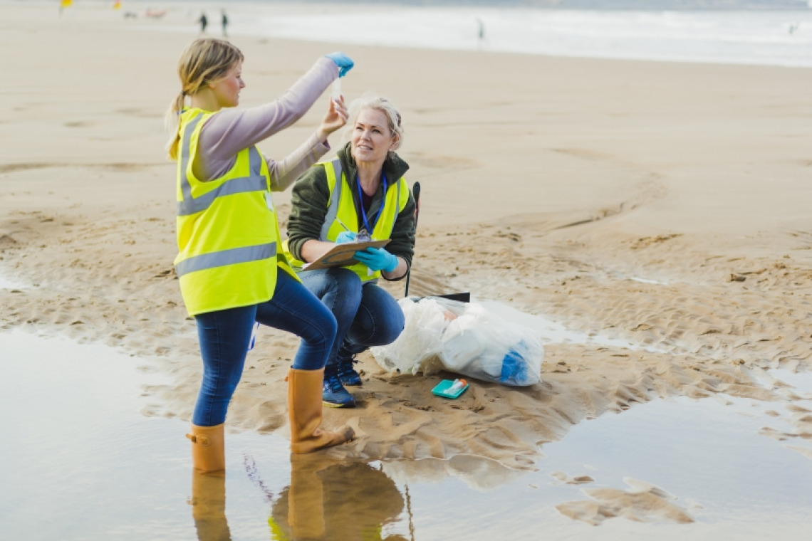 Two researchers gathering a water sample from a beach
