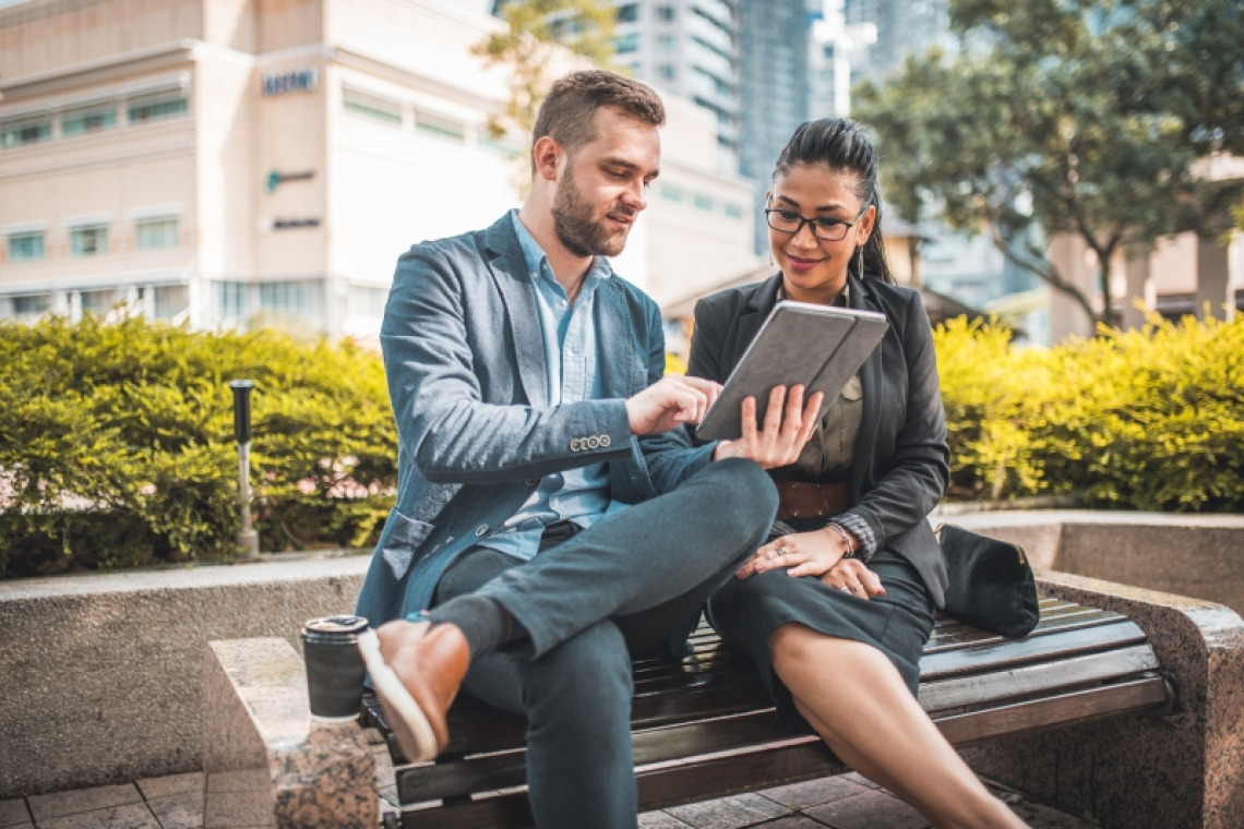 A man and woman looking at a tablet together on a park bench