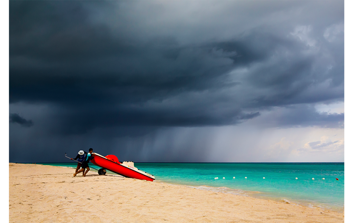 storm approaching beach where two men stand with boat