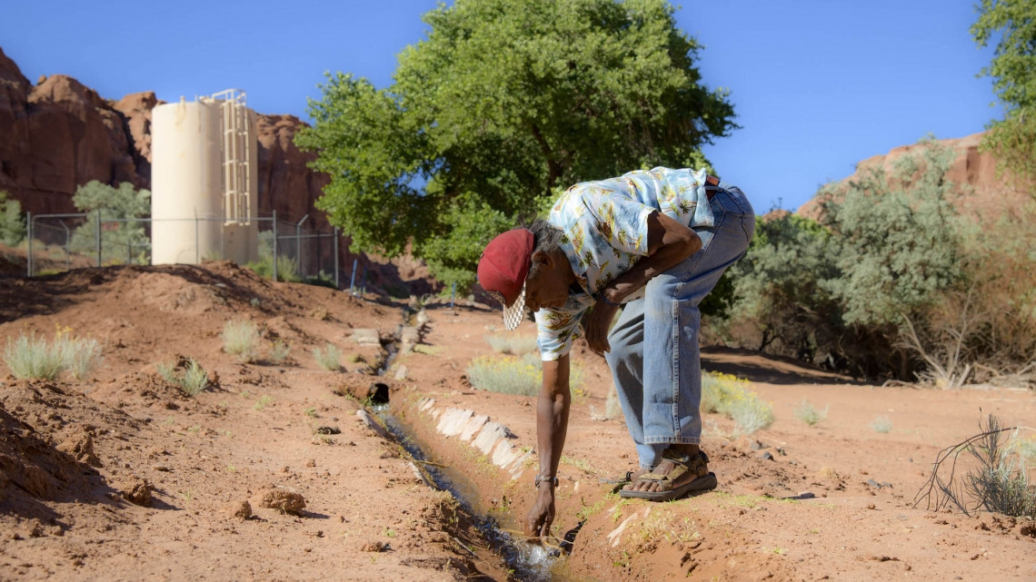 A man leaning over a small stream of water on the Navajo Nation
